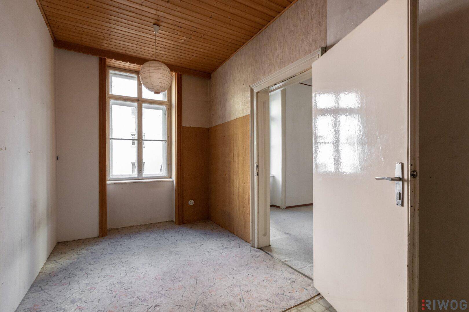 Kleineres Zimmer mit Holzdecke, einem Fenster und älterem Bodenbelag, renovierungsbedürftig.