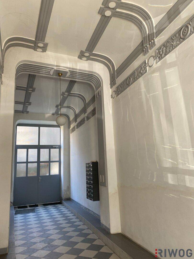 Heller Eingangsbereich mit hohen Decken, kunstvoller Stuckverzierung und Schachbrettmuster-Fliesenboden.