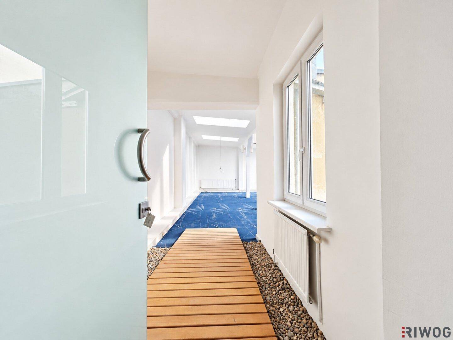 Moderner Flur mit Holzlaufsteg über blauem Teppich und dekorativen Kieselsteinen, führt zu weiteren Räumen.