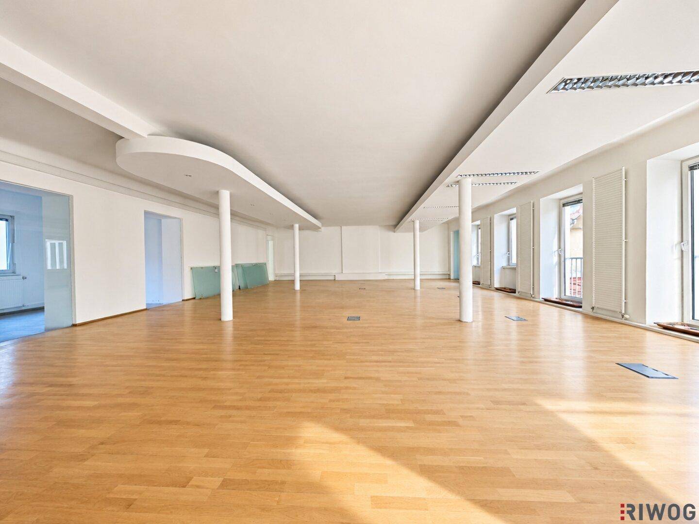 Weitläufiger Büroraum mit vielen Fenstern und Holzboden, bietet viel Tageslicht und Gestaltungsmöglichkeiten.