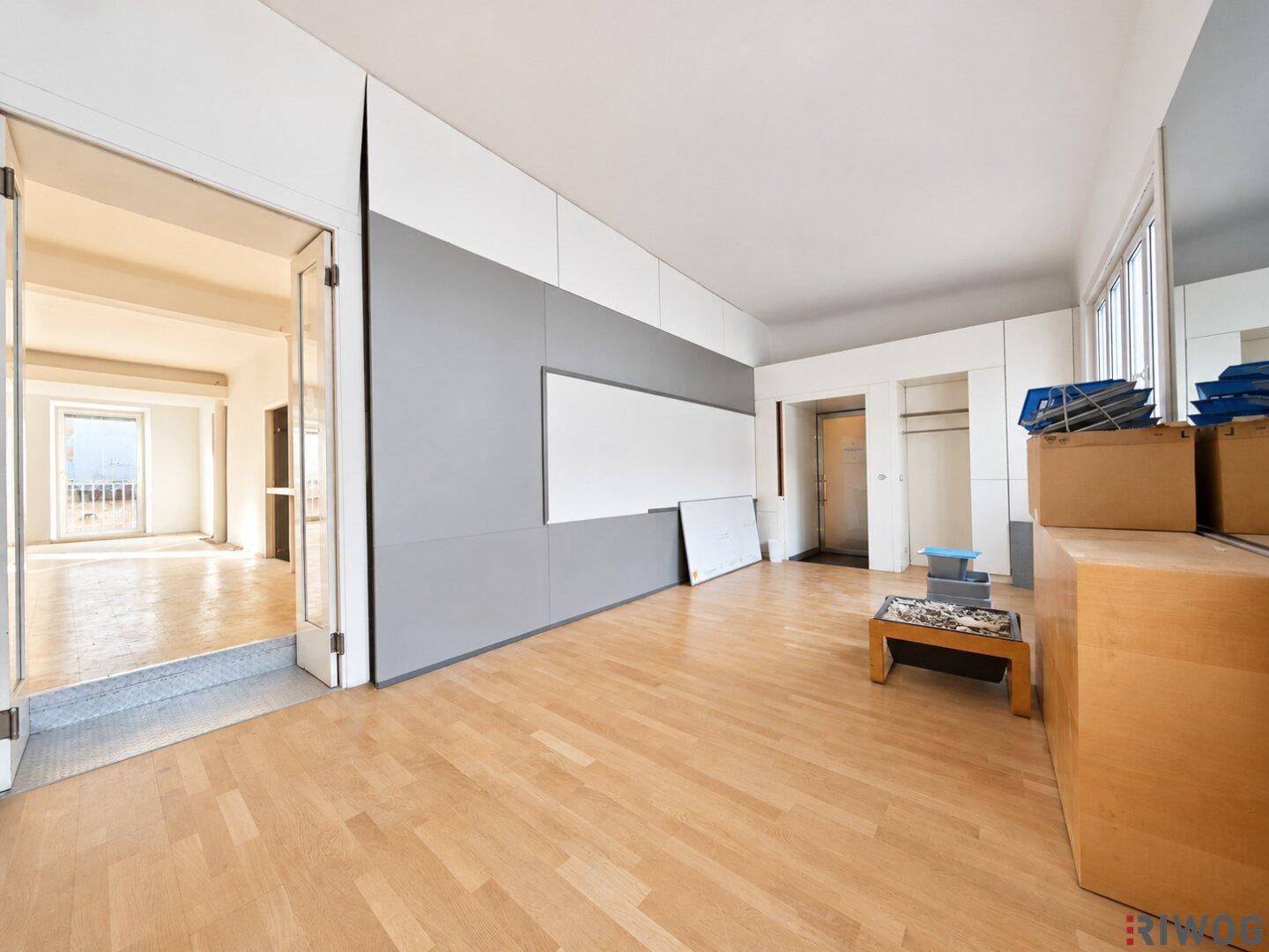 Heller Büroraum mit Holzboden und modernen grauen Wandpaneelen, bietet vielseitige Nutzungsmöglichkeiten.