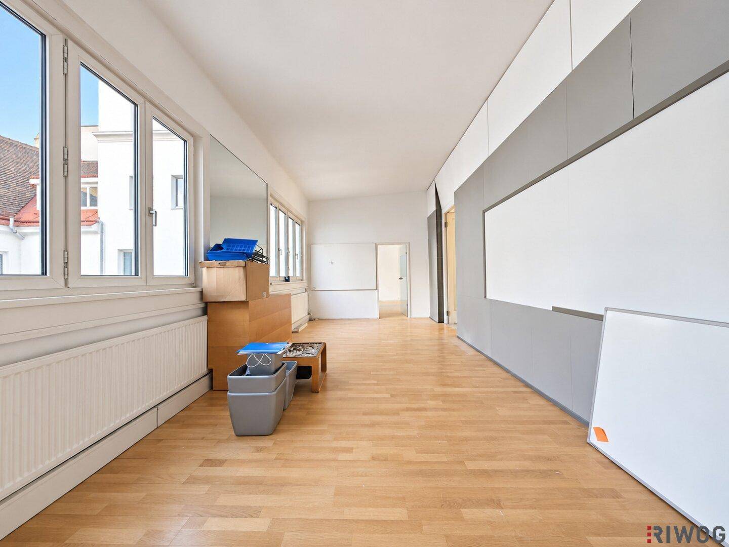 Geräumiger Büroraum mit Holzboden und großen Fenstern, die viel Tageslicht hereinlassen.