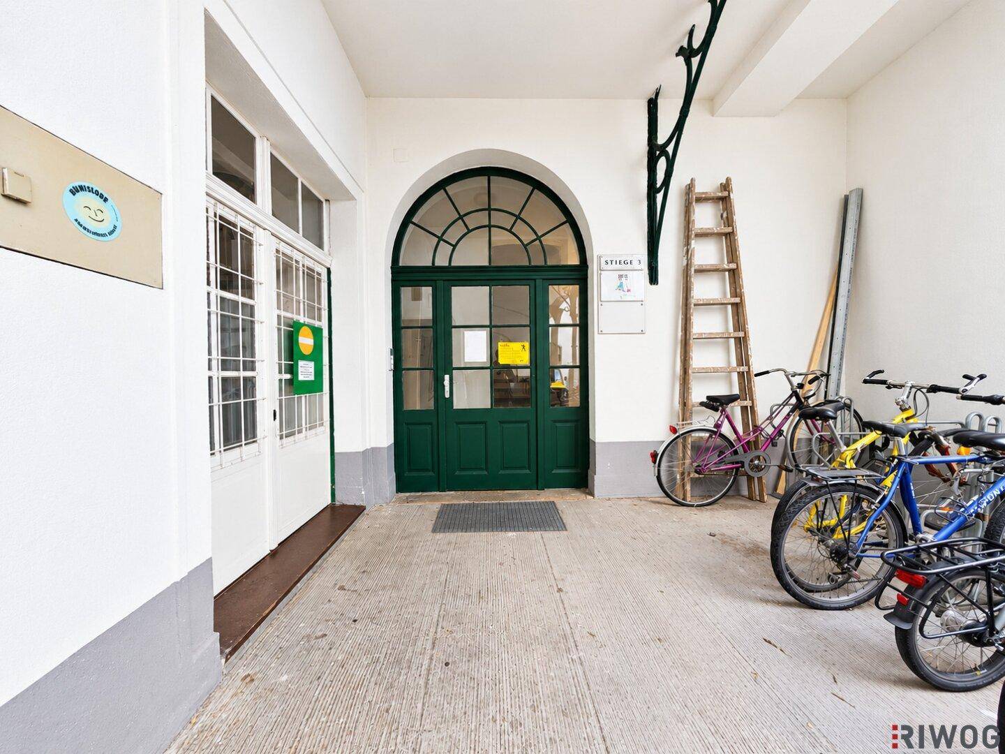Überdachter Eingangsbereich mit grüner Bogentür und Fahrradabstellmöglichkeiten.