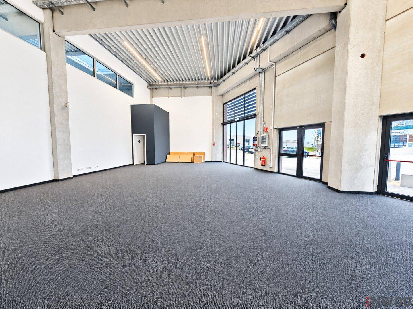 Geräumiger, heller Bürobereich mit Teppichboden, hohen Decken und großen Fensterfronten.