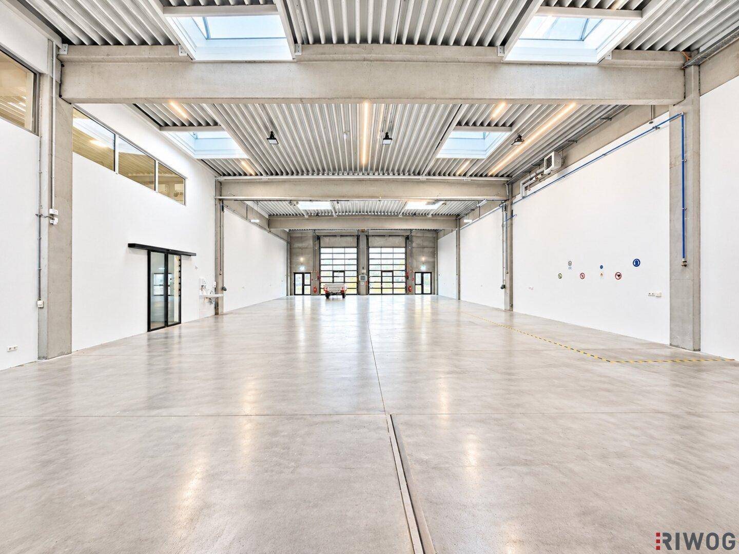 Große Lagerhalle mit Betonboden, hohen Decken, Oberlichtern und zwei großen Rolltoren.