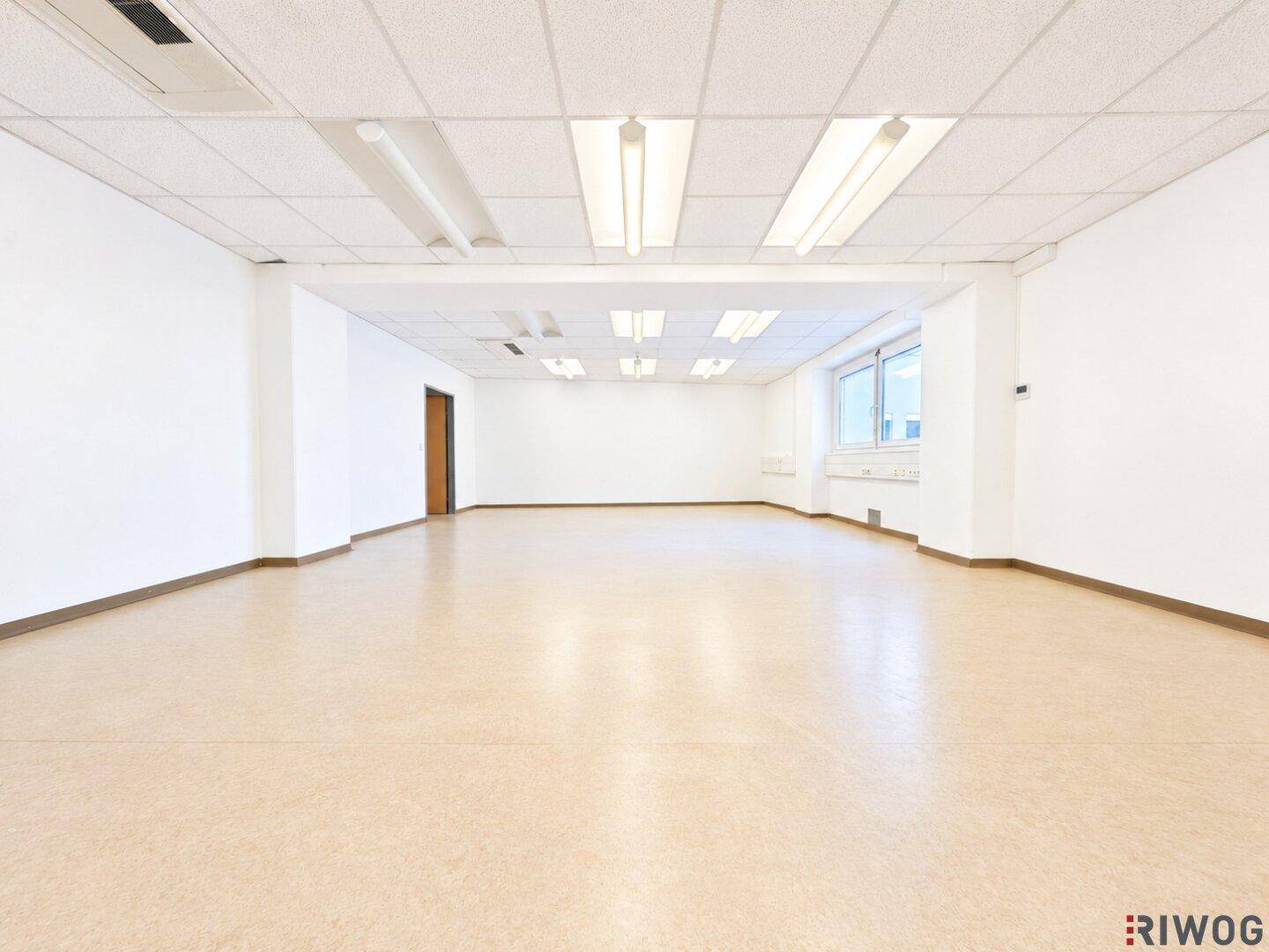 Weitläufiger Bürobereich mit zahlreichen Deckenleuchten und durchgehenden Fenstern.