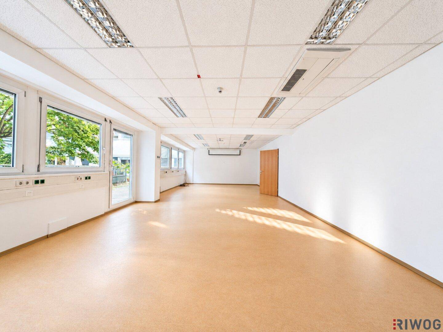 Geräumiger, heller Büroraum mit großen Fenstern und Zugangstür, ideal für Großraumbüros.