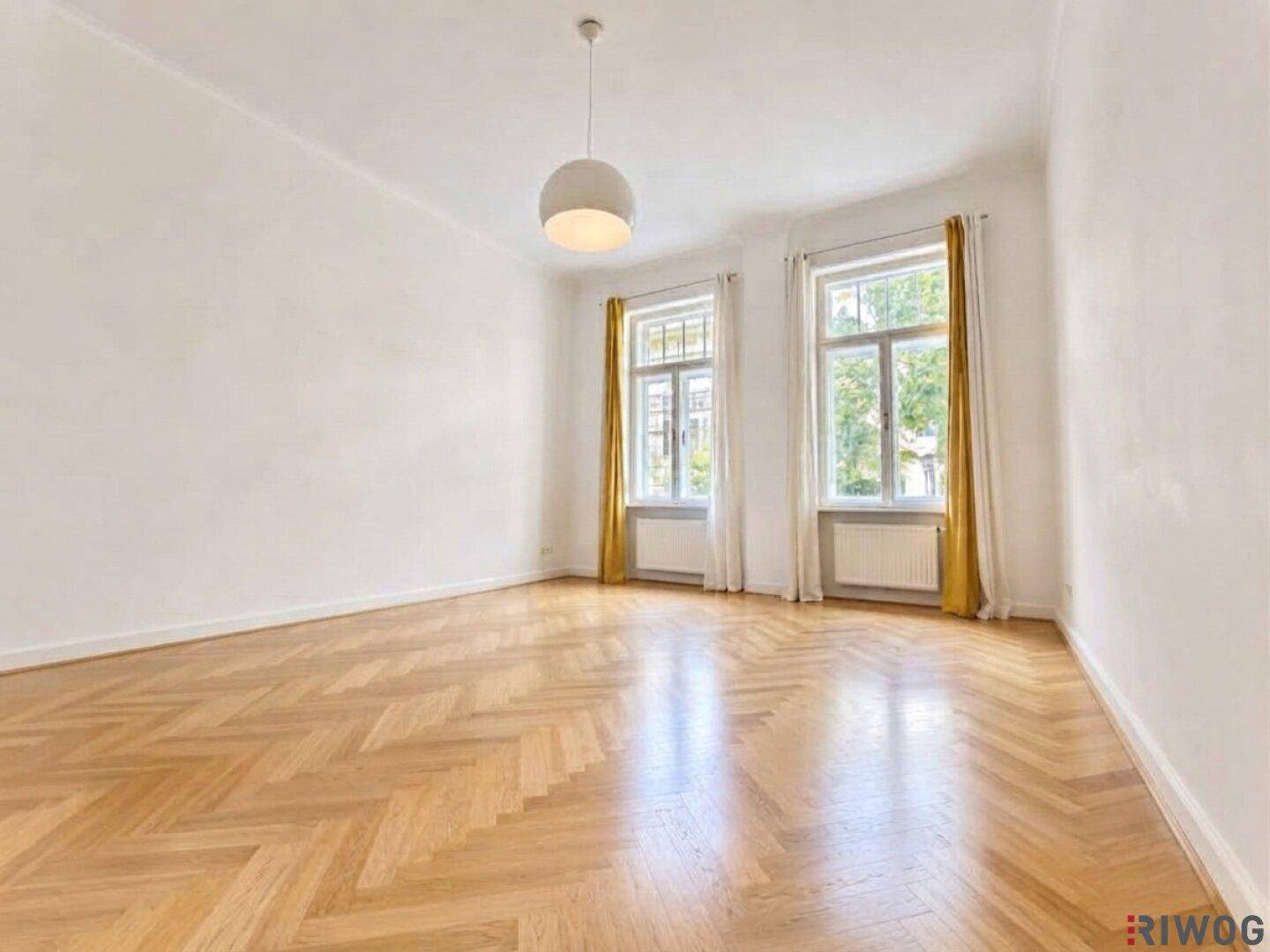 Heller Raum mit Fischgrätparkett, zwei großen Fenstern und einer modernen Deckenleuchte.