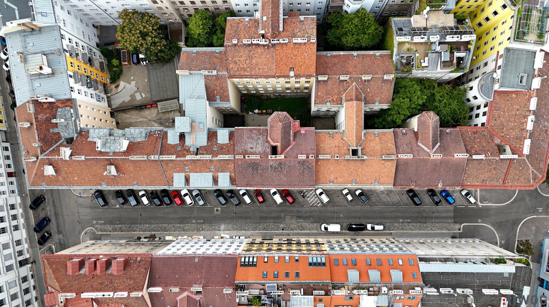 Luftaufnahme einer städtischen Bebauung mit roten Dächern, Innenhof und Parkplätzen.