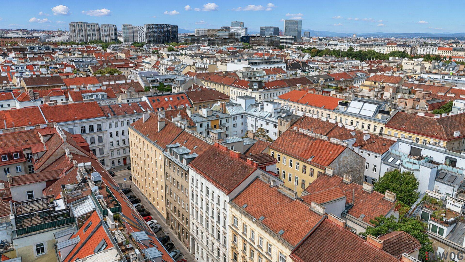 Weitläufiger Blick über die Dächer einer dicht bebauten Stadt mit Hochhäusern im Hintergrund.