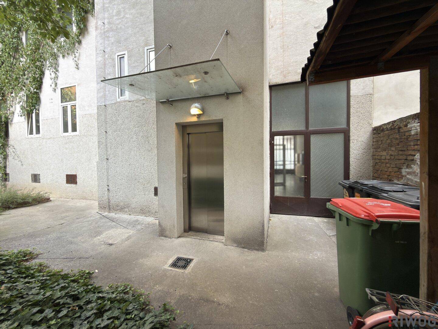 Blick auf den Aufzugseingang im Innenhof eines Altbaus mit Fahrradunterstand.