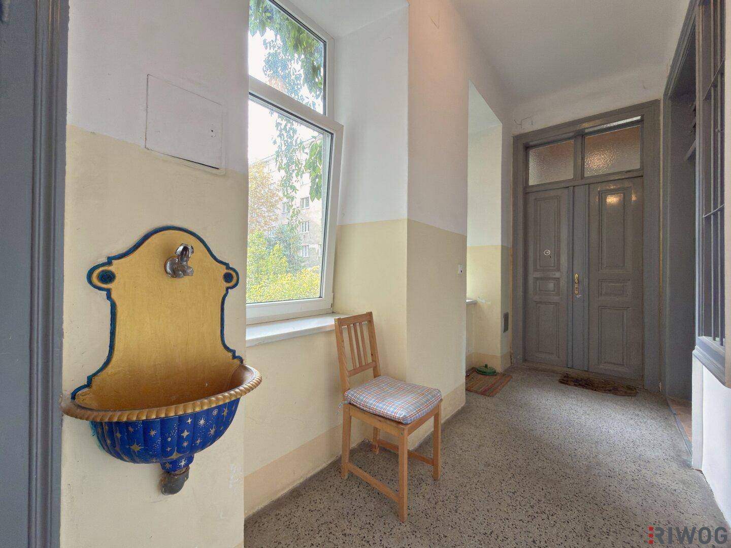 Historischer Hausflur mit dekorativem Wandbrunnen, großem Fenster und Terrazzoboden.