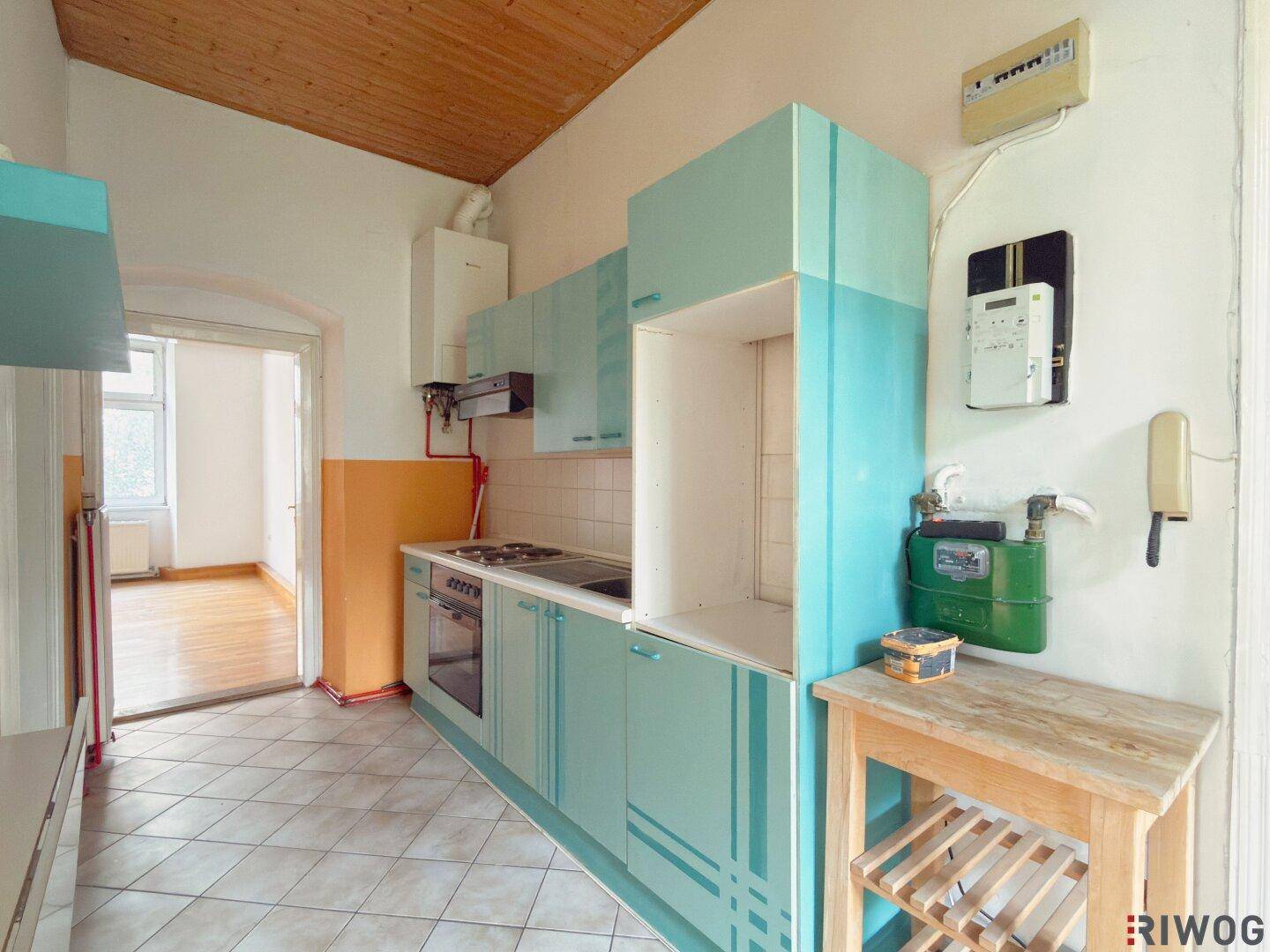 Küche mit hellblauen Schränken, Fliesenboden und Blick in einen angrenzenden Raum mit Holzboden.