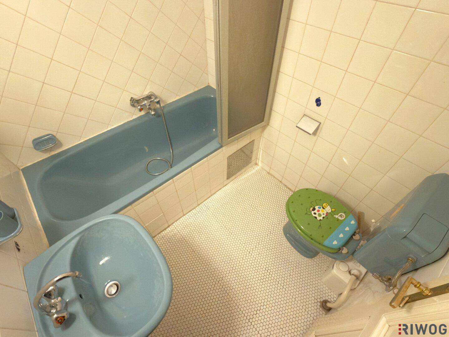 Badezimmer mit blauer Badewanne, Waschbecken und WC, gefliest mit kleinen Mosaikfliesen.
