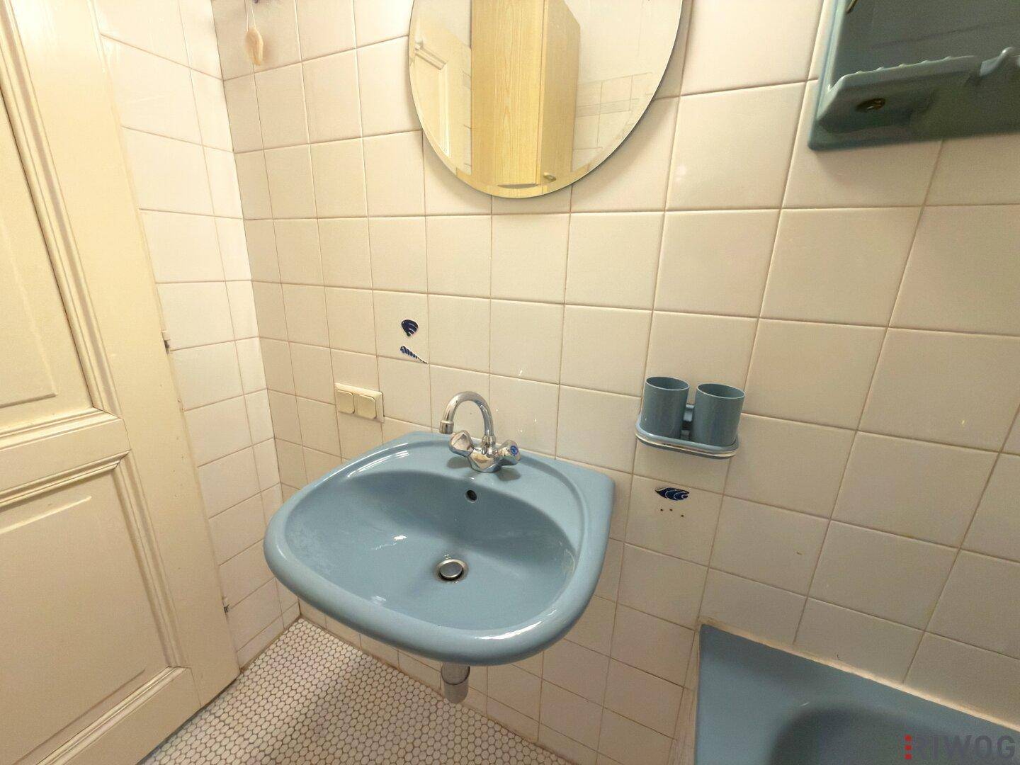 Waschbecken in Hellblau mit Spiegel und Fliesen an den Wänden im Badezimmer.