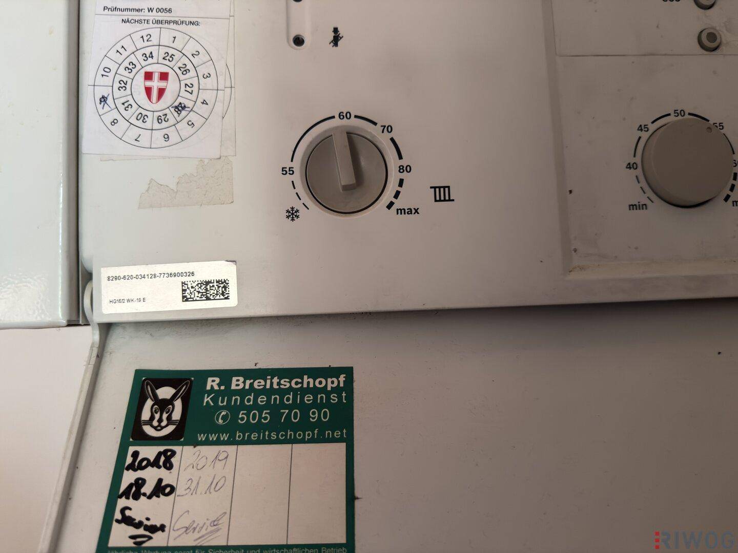 Nahaufnahme der Steuerung einer Gastherme mit Wartungsaufklebern und Temperatureinstellungen.