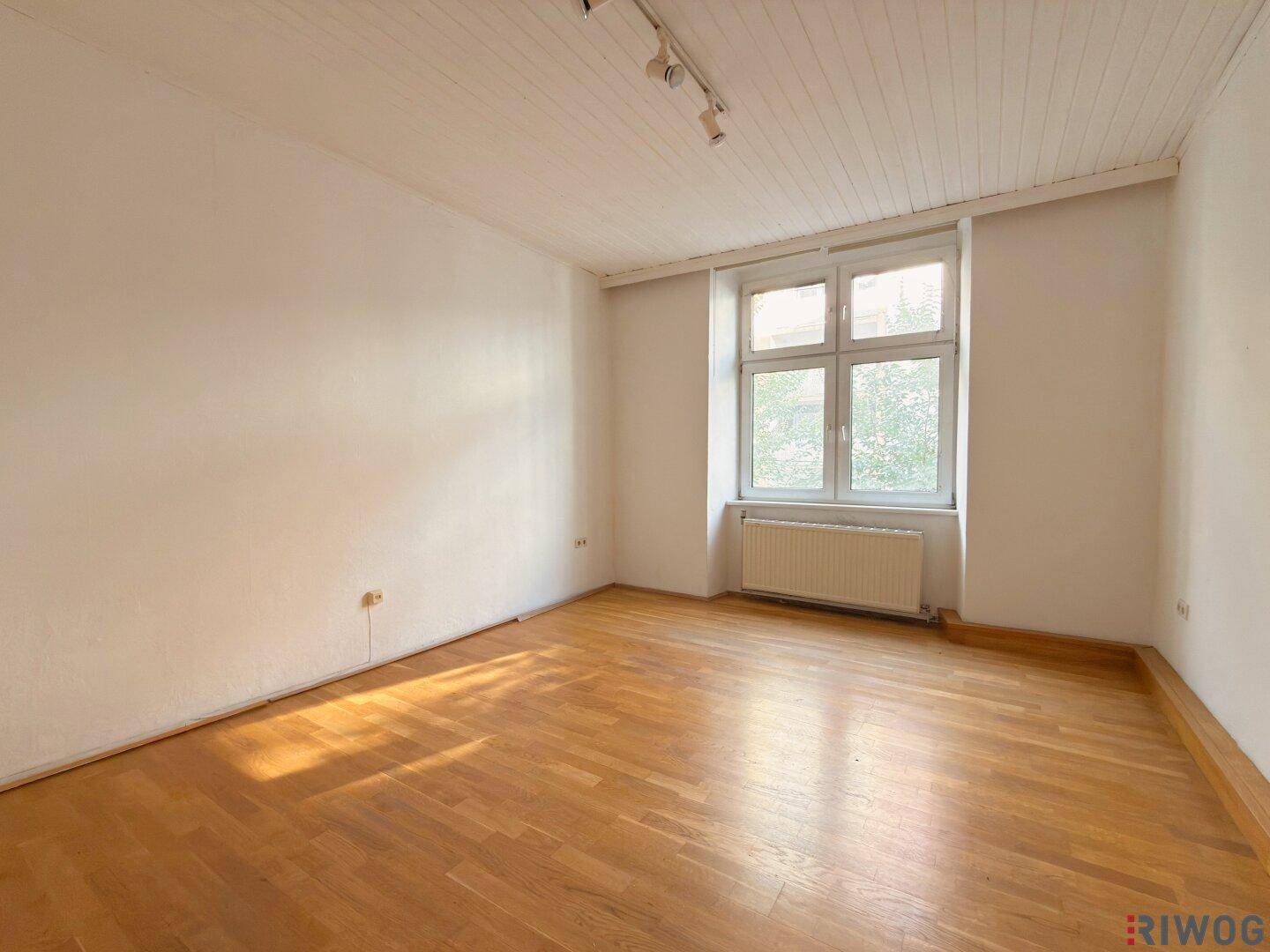 Lichtdurchfluteter Raum mit Holzboden und einem großen Fenster, das viel Tageslicht hereinlässt.