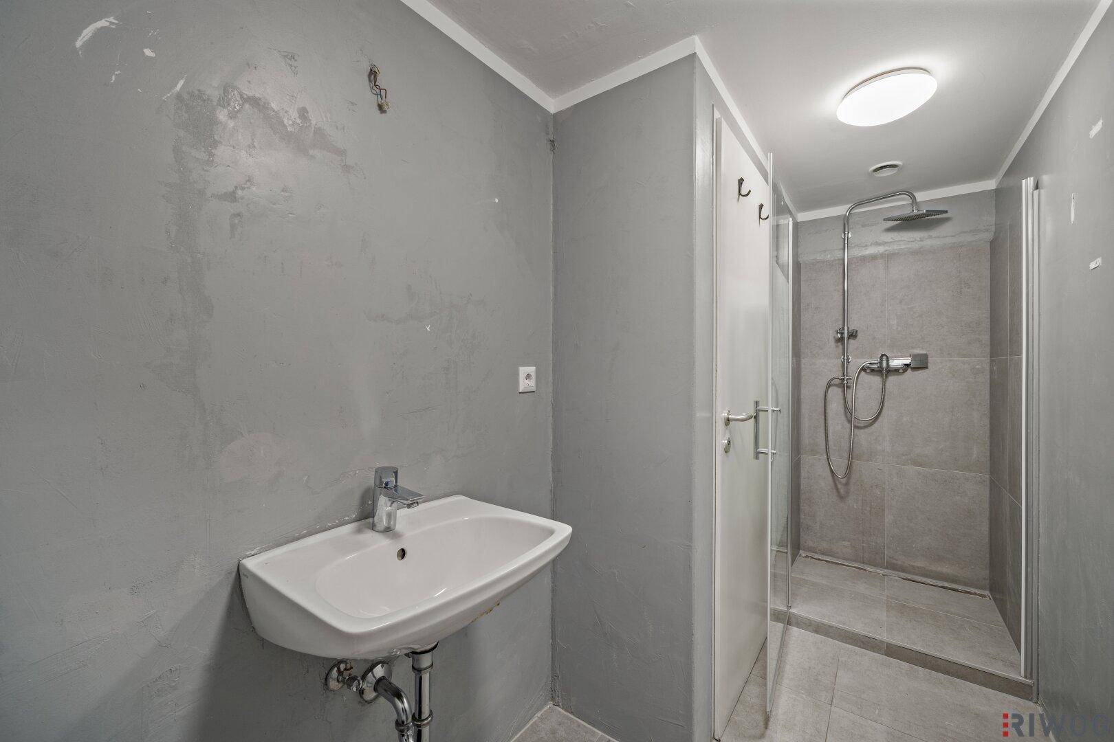 Funktionales Badezimmer mit Waschbecken und Duschkabine, ausgestattet mit grauen Fliesen.