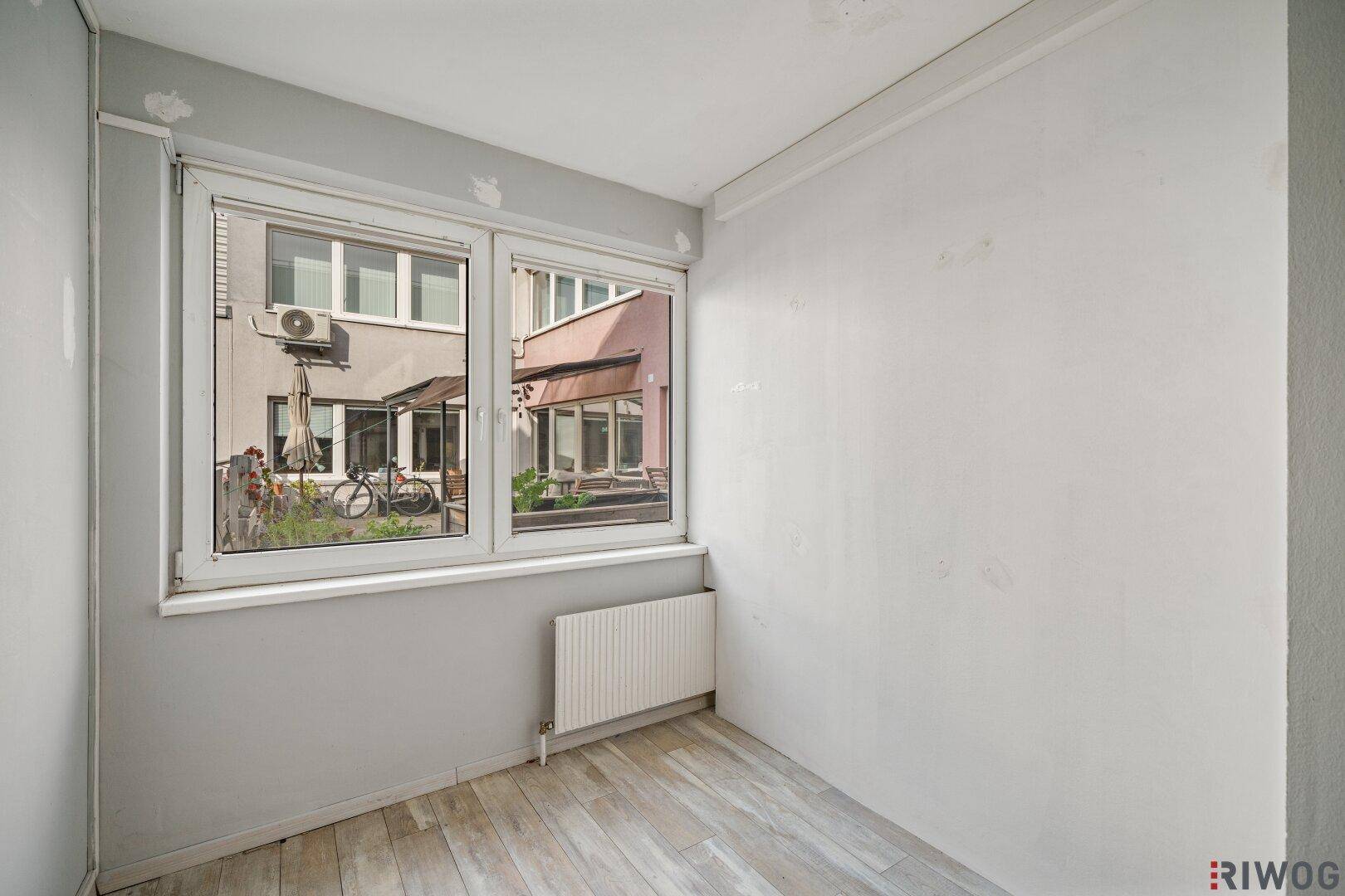 Kleiner Raum mit hellem Boden und Fenster, das einen Blick auf den Innenhof bietet.