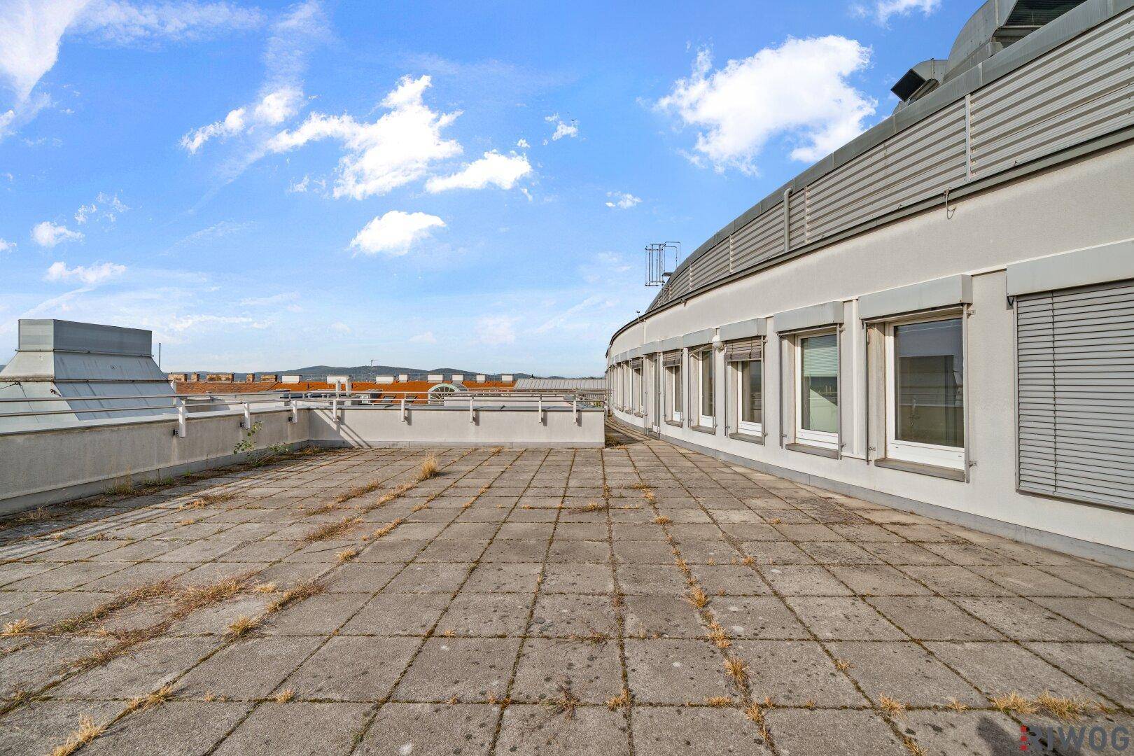 Weitläufige Dachterrasse mit Blick auf die Gebäudefassade und die städtische Umgebung.