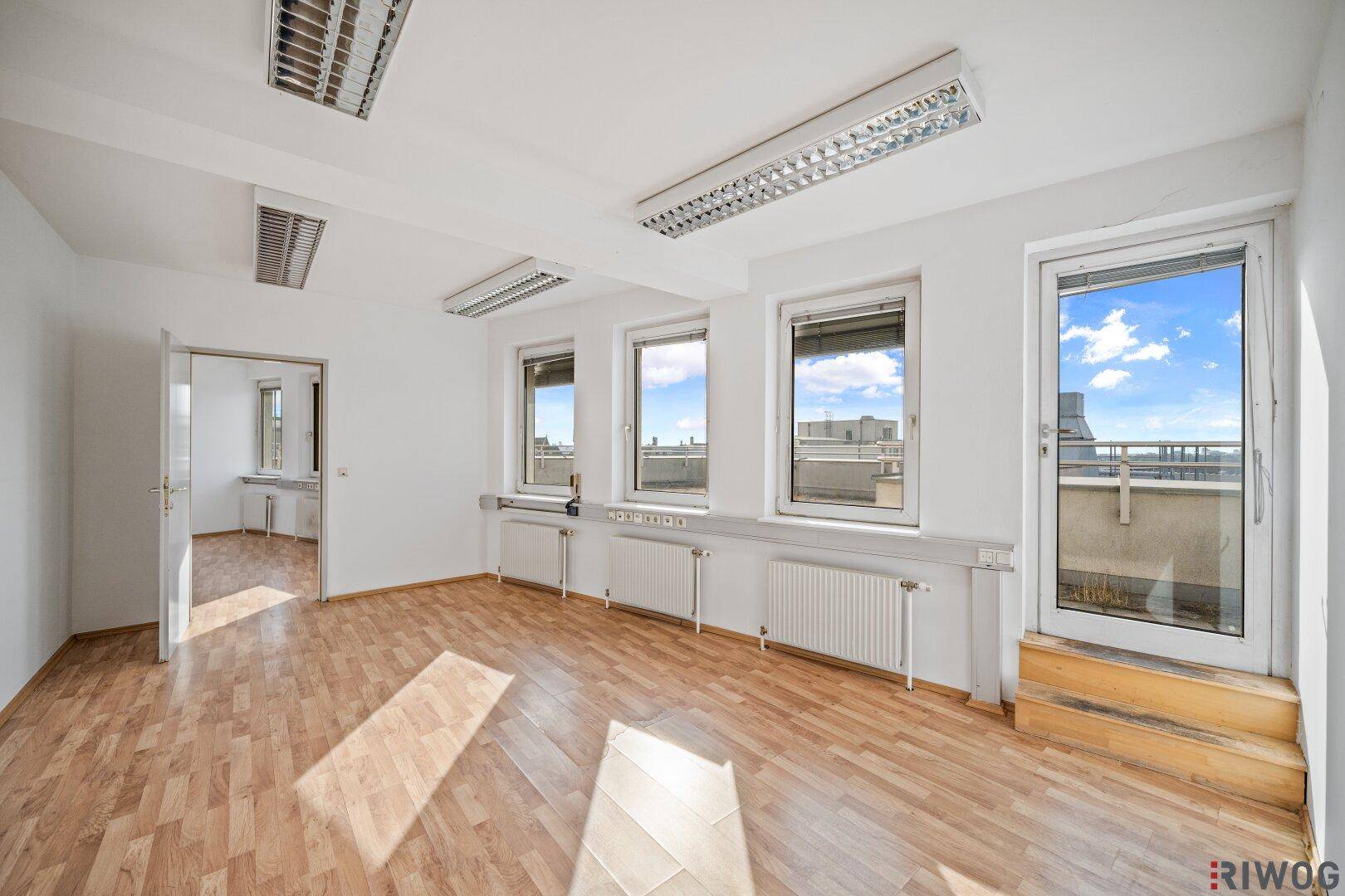 Büroraum mit Laminatboden, großen Fenstern und direktem Zugang zu einem Außenbereich.