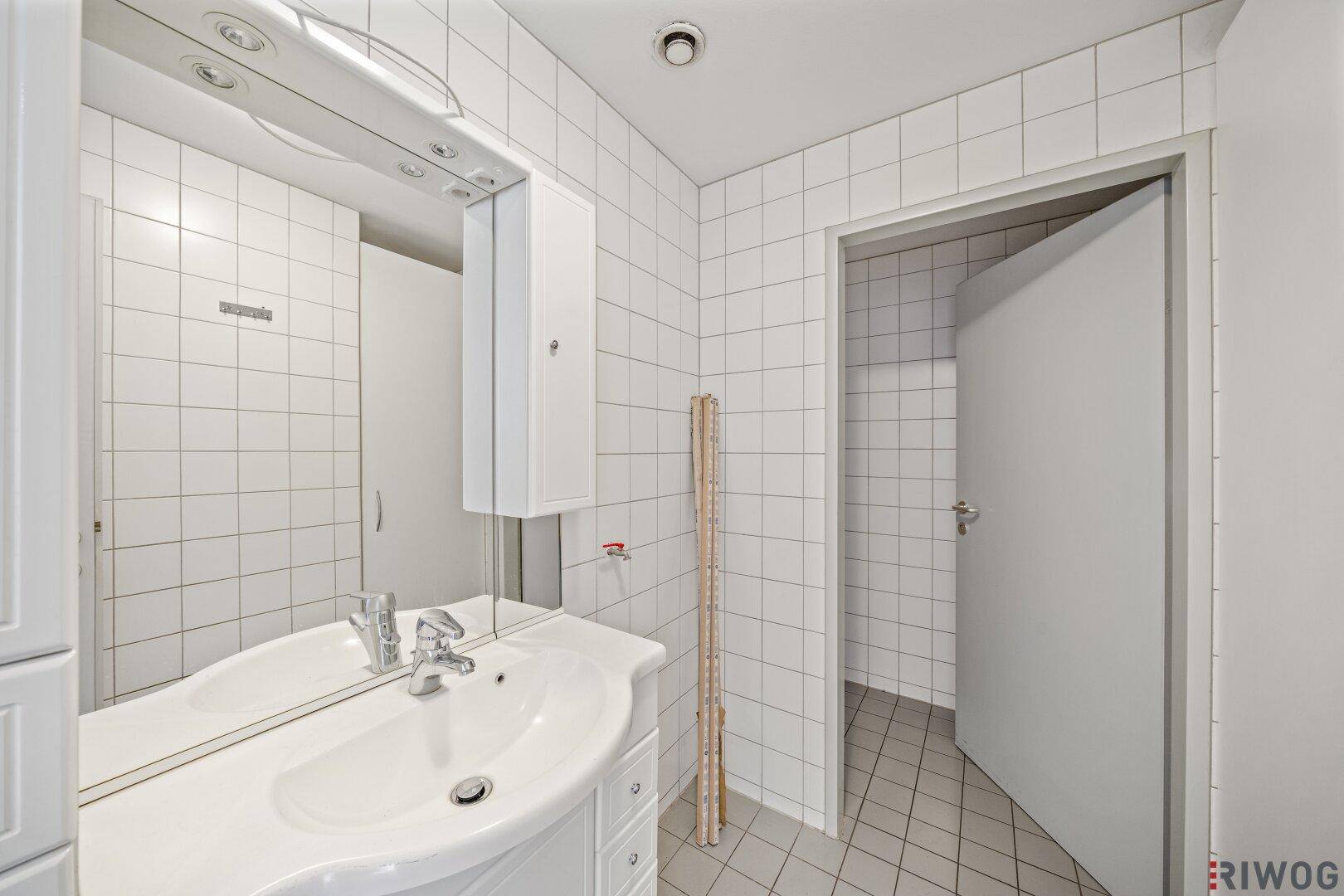 Badezimmer mit weißem Waschbecken, großem Spiegel und weißen Wandfliesen.