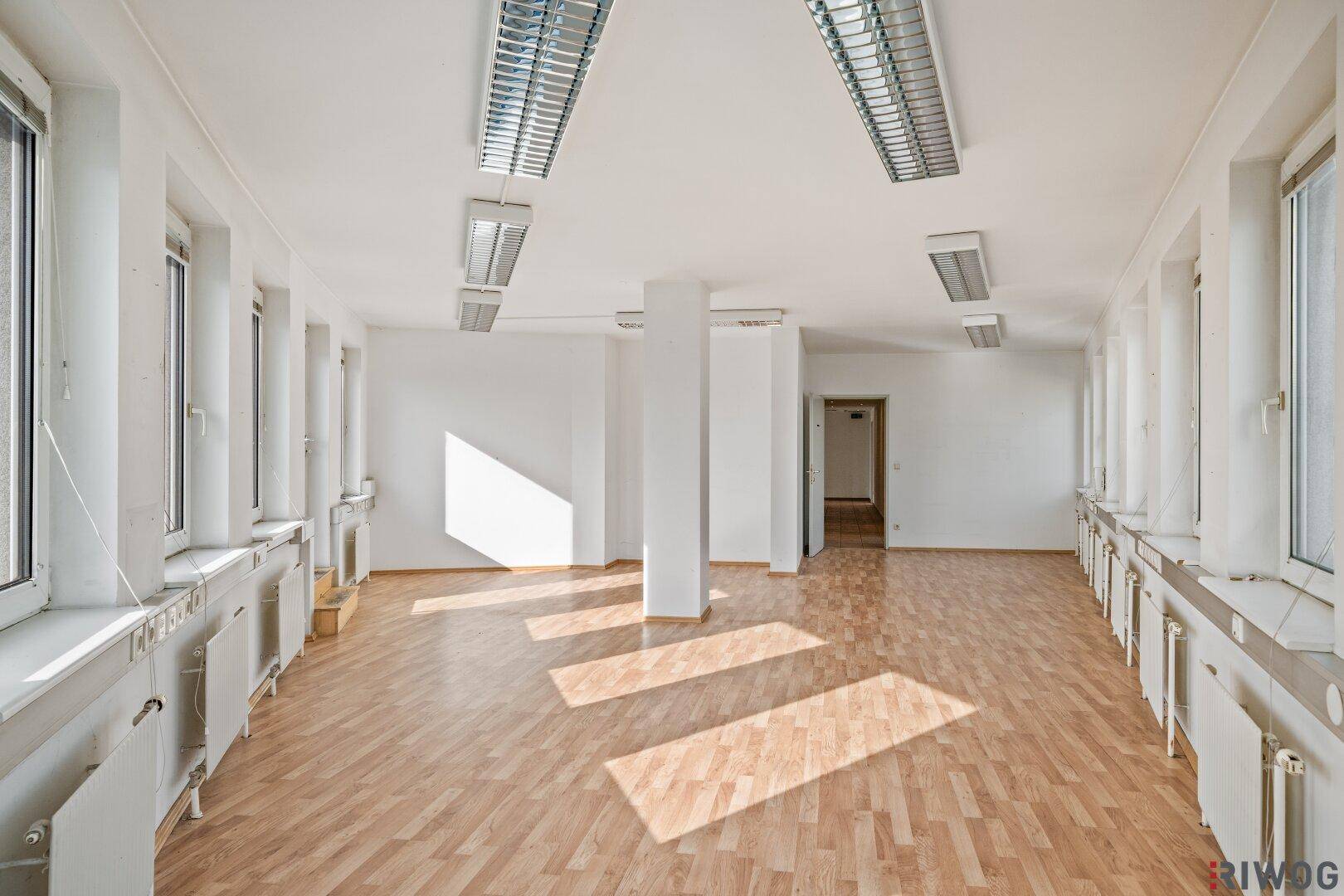 Geräumiger Bürobereich mit Säulen, Laminatboden und viel Tageslicht durch die Fenster.
