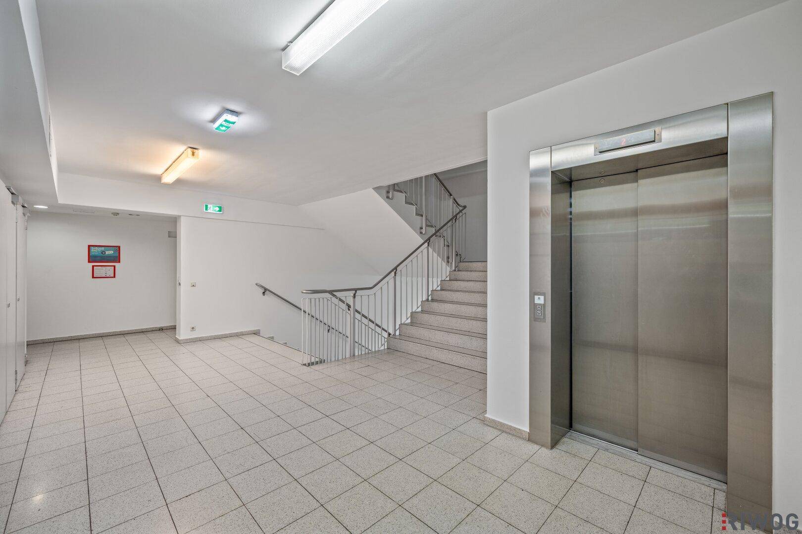 Gemeinschaftsbereich mit Treppenhaus, Aufzug und gefliestem Boden in einem modernen Gebäude.