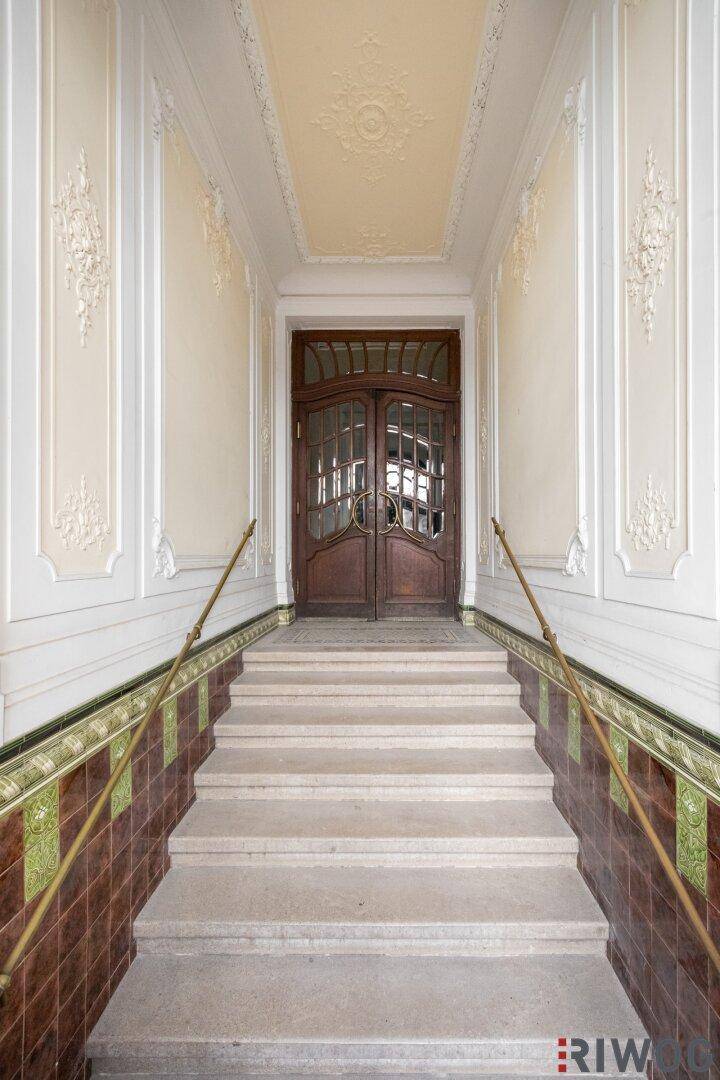 Historisches Treppenhaus mit aufwendigen Stuckverzierungen und einer eleganten Holztür am Ende des Ganges.