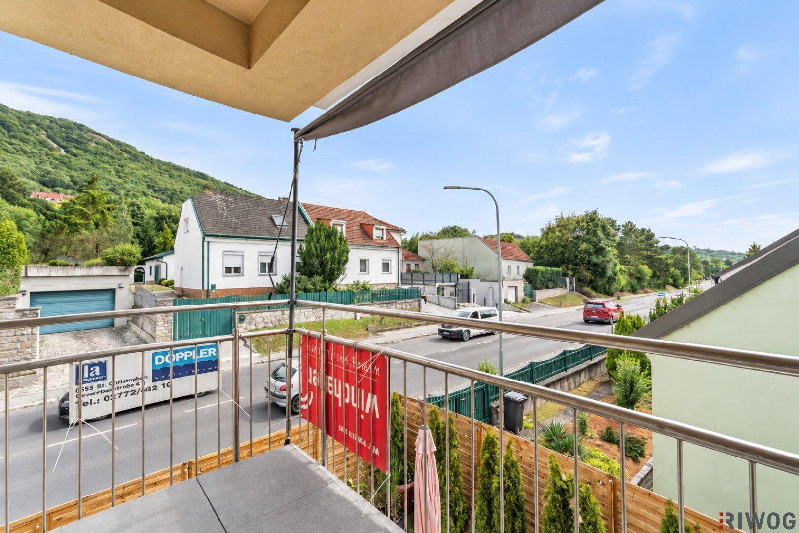 Balkon mit Blick auf die Straße, umliegende Häuser und eine grüne Hügellandschaft.