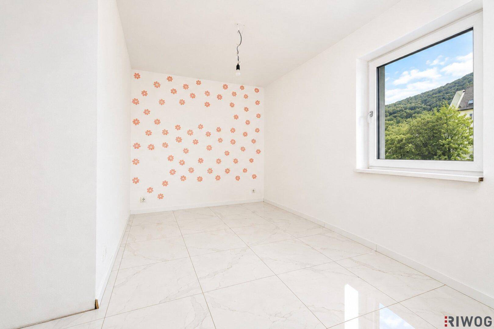 Helles Zimmer mit weißen Wänden, floralen Dekorationen und einem Fenster mit Bergblick.