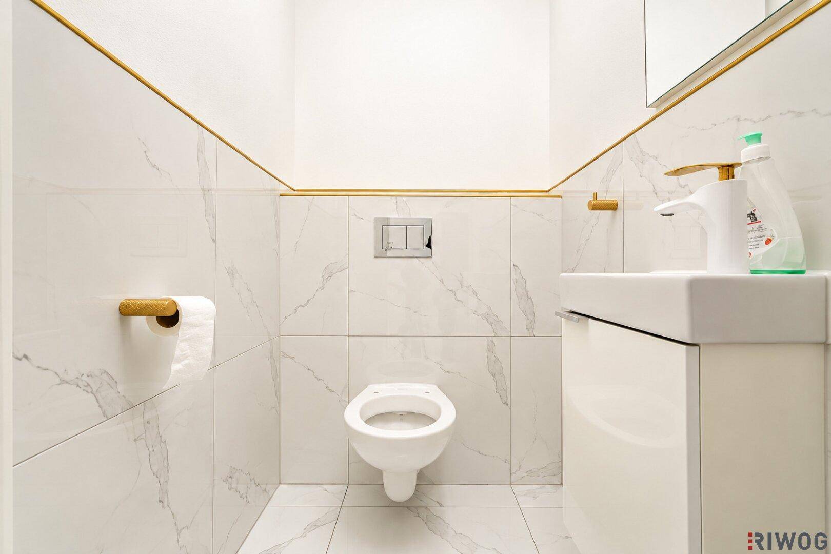 Stilvolles Gäste-WC mit weißen Marmorfliesen, goldenen Akzenten und wandhängendem WC.