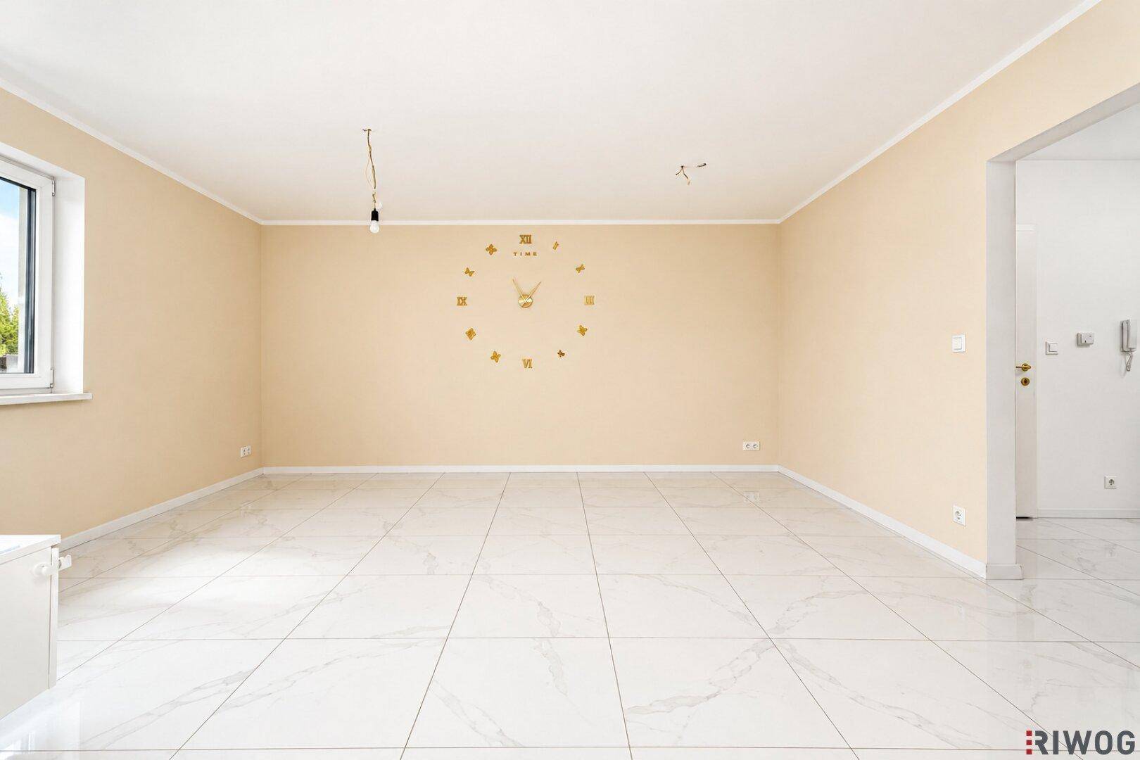 Geräumiges, helles Zimmer mit beigefarbenen Wänden und glänzenden Fliesen, bereit zur Einrichtung.