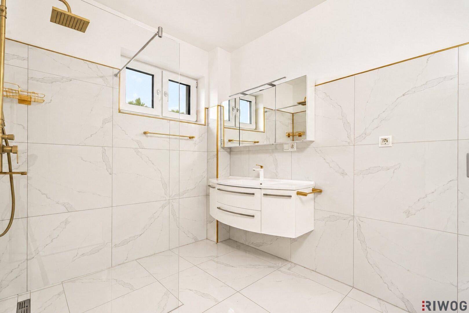 Elegantes Badezimmer mit goldfarbenen Details, großformatigen Fliesen und einem modernen Waschtisch.