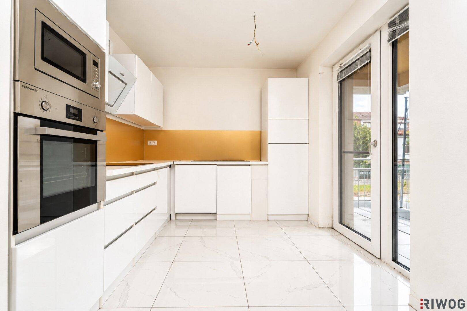 Moderne weiße Einbauküche mit integrierten Geräten, goldenem Spritzschutz und Zugang zum Außenbereich.