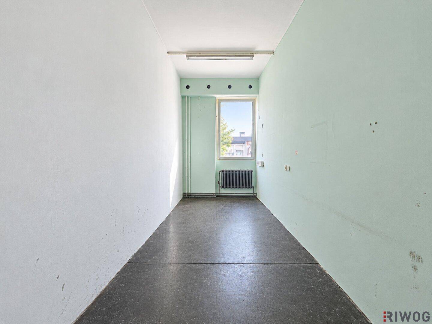 Schmaler Raum mit hellgrüner Wand, Fenster und Heizkörper, geeignet als Abstellraum.