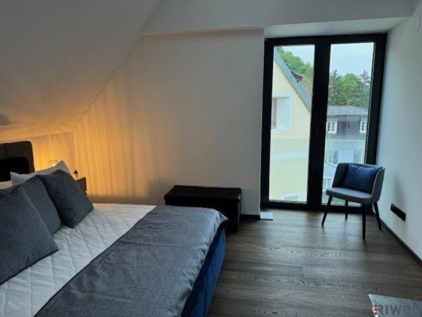 Schlafzimmer mit großem Fenster, Holzboden und Dachschräge, bietet Zugang nach draußen.