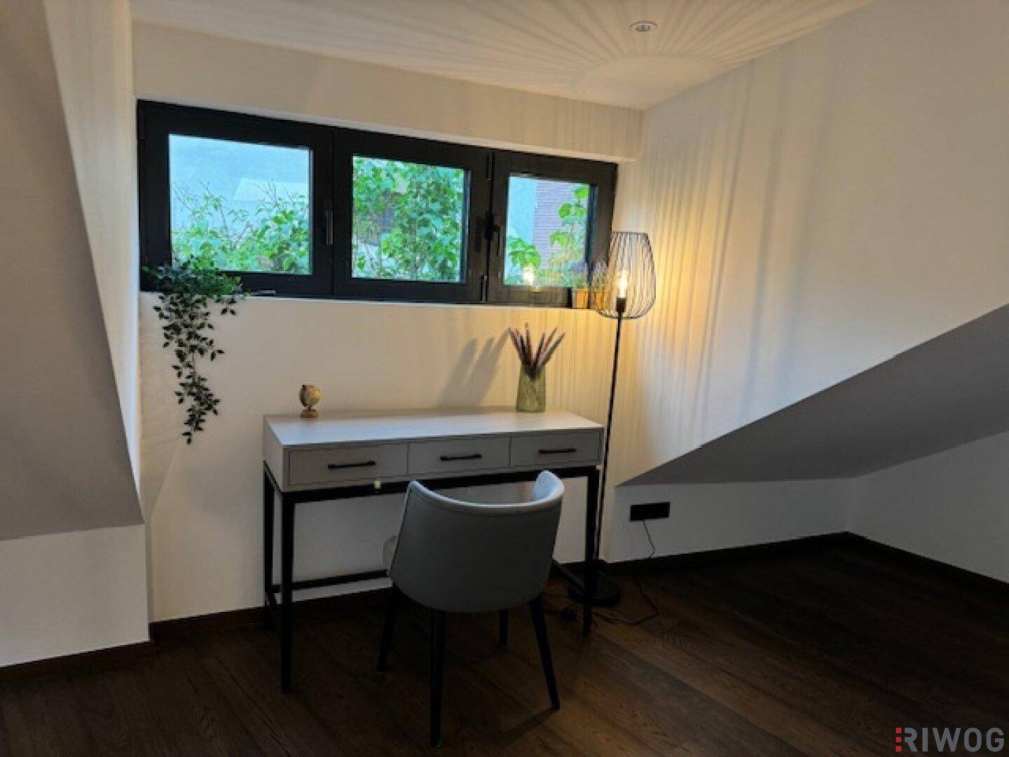 Arbeitsbereich mit Schreibtisch, Stuhl und Fenstern unter einer Dachschräge.