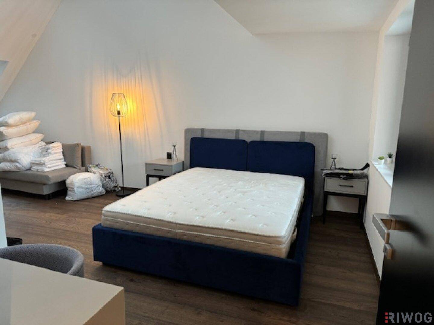 Helles Schlafzimmer mit Doppelbett, Sofa und stilvoller Stehlampe auf Holzboden.