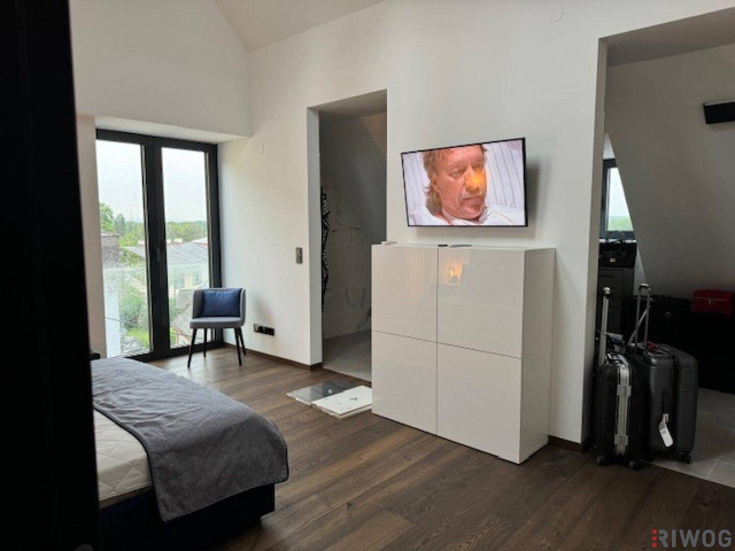 Schlafzimmer mit Doppelbett, weißem Schrank und großem Fenster mit Blick ins Grüne.