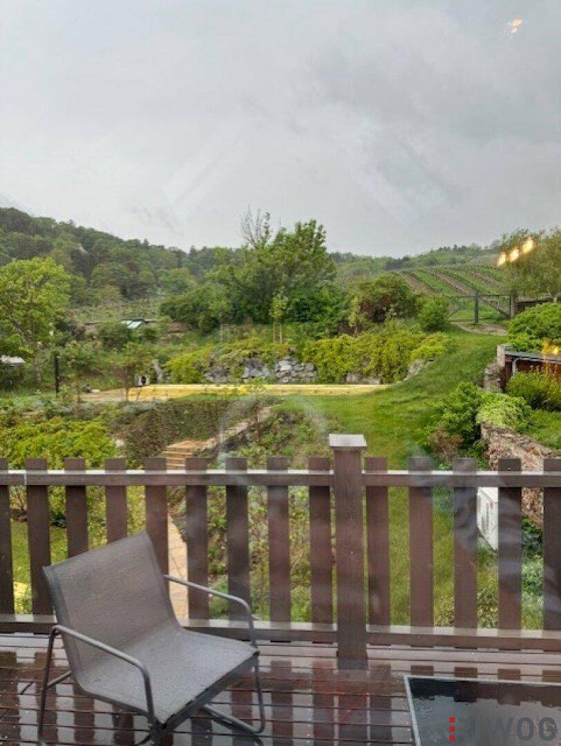 Balkon mit Sitzgelegenheiten und weitem Blick auf grüne Weinberge unter bewölktem Himmel.