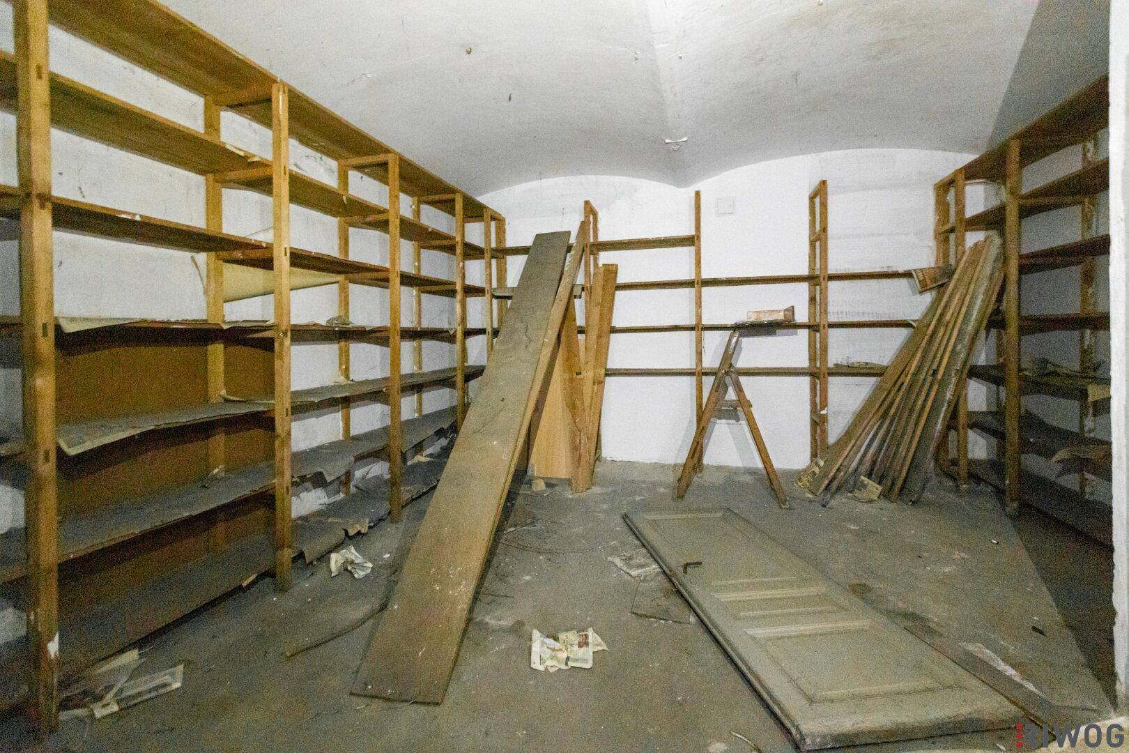 Großer, leerer Lagerraum mit vielen Holzregalen und gewölbter Decke, in sanierungsbedürftigem Zustand.