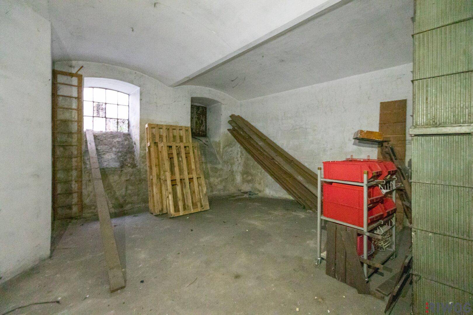 Unaufgeräumter Lagerraum mit Holzpaletten, Brettern und einem kleinen Fenster, in sanierungsbedürftigem Zustand.