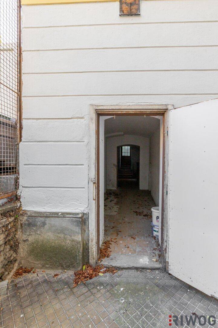 Eingang zum Kellergeschoss von außen, mit offener Tür und Blick in einen langen Gang.