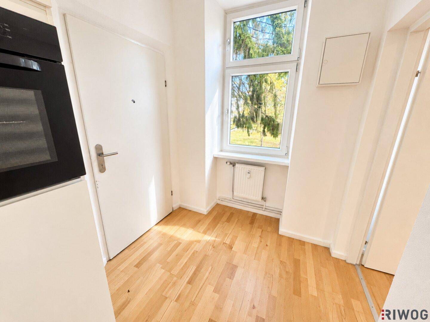 Leerer Küchenbereich mit Parkettboden, Fenster und Vorbereitung für Einbaugeräte.