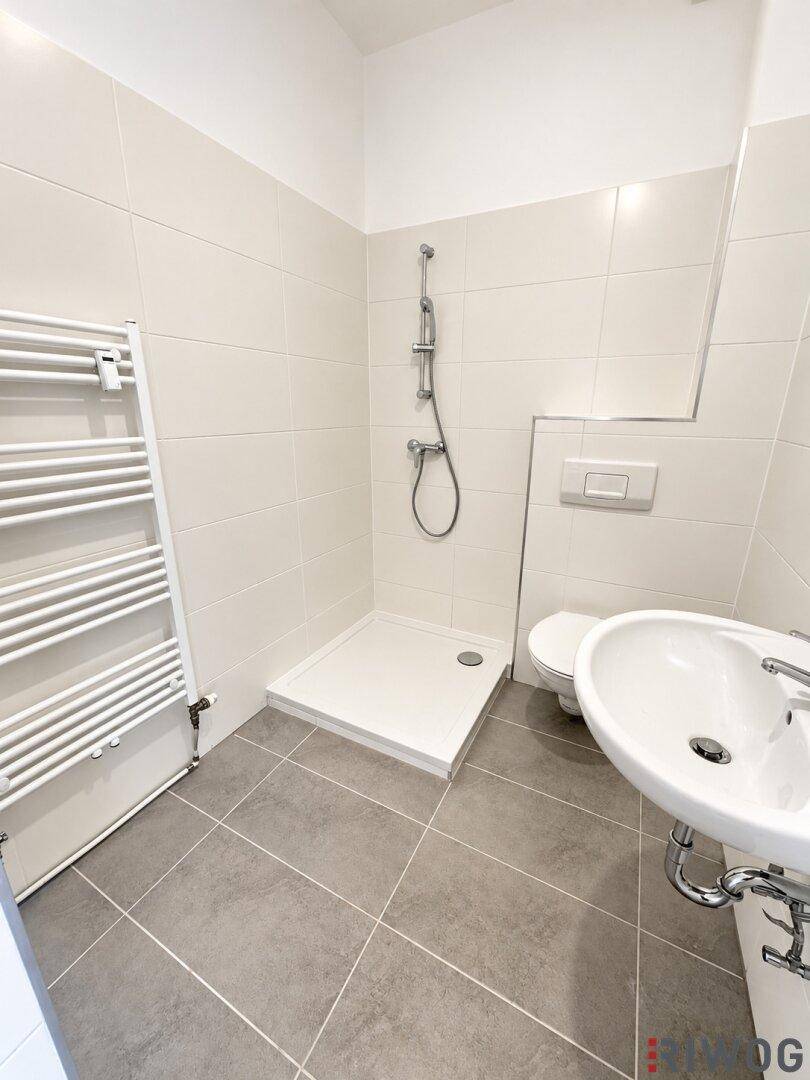 Helles Badezimmer mit Dusche, WC, Waschbecken und beheiztem Handtuchhalter.