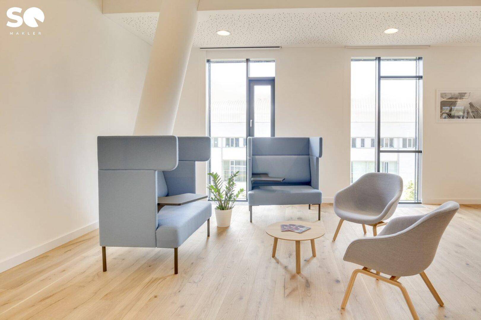 Gemütlicher Loungebereich mit modernen blauen Sitzmöbeln, Holzboden und großen Fenstern.