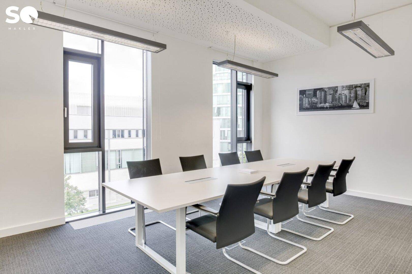 Moderner Konferenzraum mit großem Tisch, schwarzen Stühlen und Teppichboden.