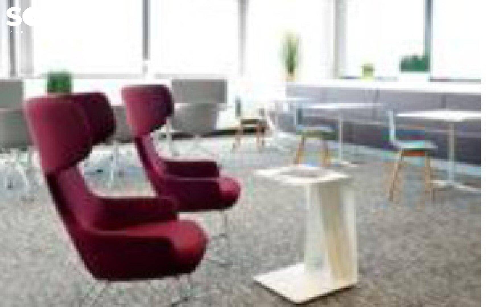 Verschwommene Aufnahme eines modernen Büroloungebereichs mit bequemen roten Sesseln und Teppichboden.