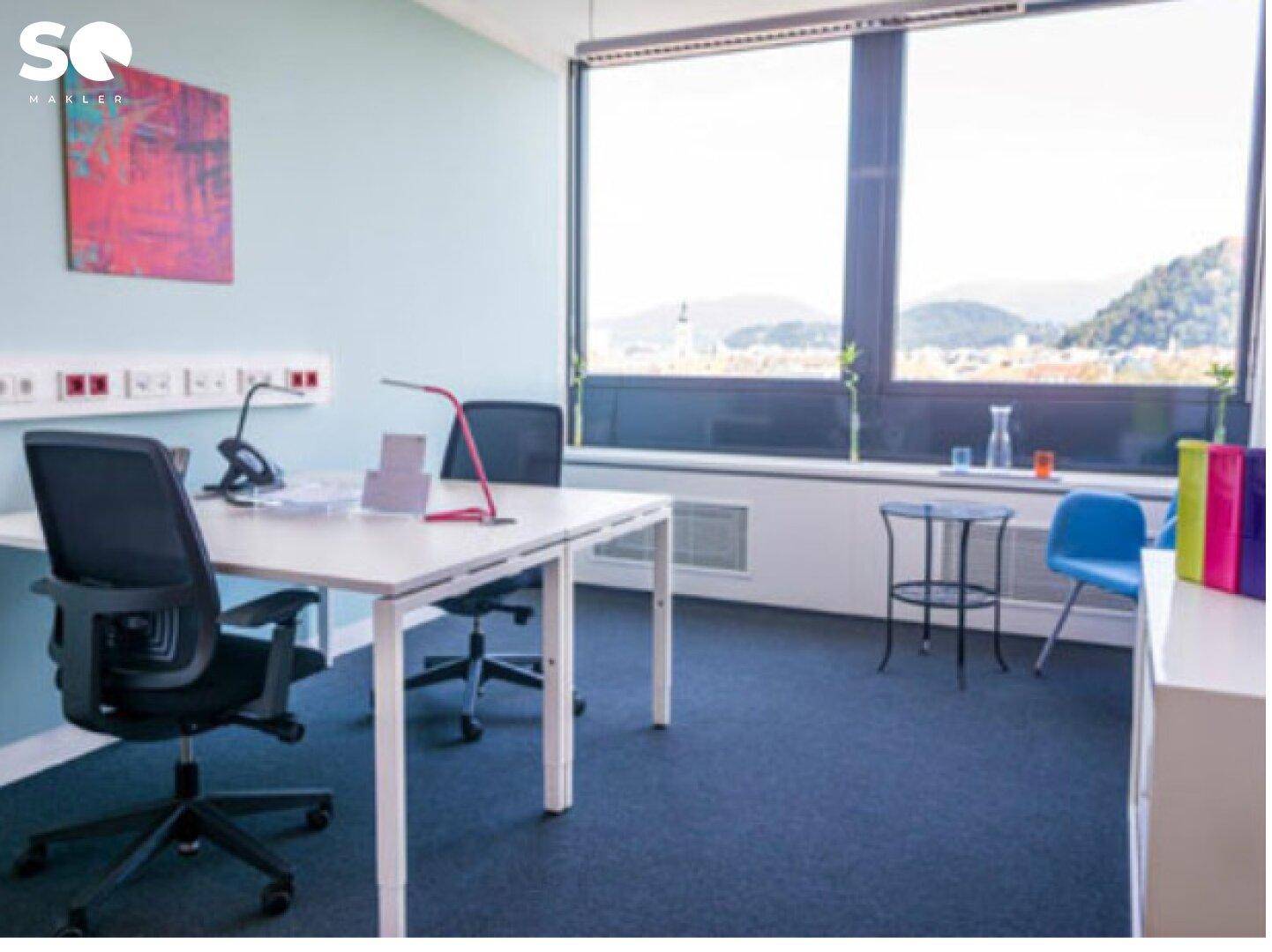 Einzelbüro mit großem Fenster, das einen weiten Blick auf die Stadt und Berge bietet.